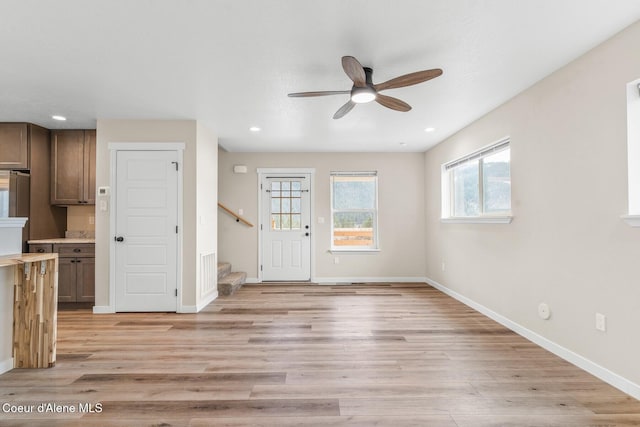 foyer featuring light wood-style floors, baseboards, stairway, and ceiling fan