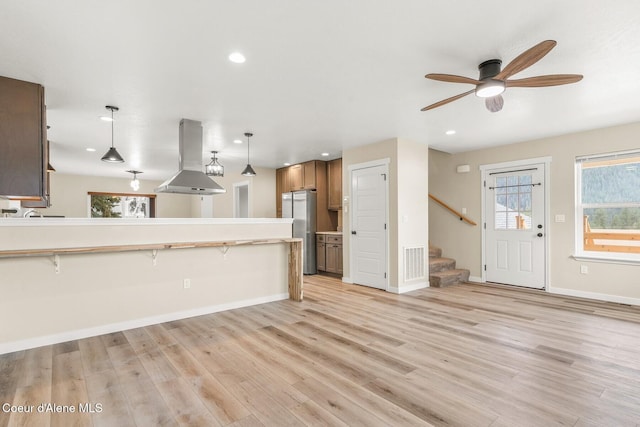 kitchen with island range hood, freestanding refrigerator, a peninsula, light wood-style floors, and pendant lighting