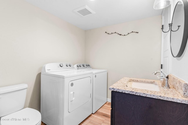 laundry area with laundry area, light wood finished floors, visible vents, washer and clothes dryer, and a sink