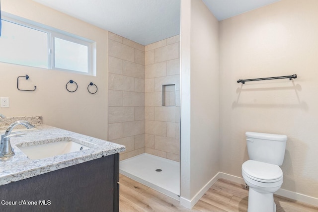 bathroom featuring baseboards, tiled shower, toilet, and wood finished floors