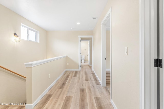 hall featuring visible vents, baseboards, light wood finished floors, and an upstairs landing