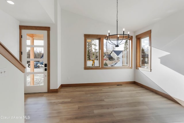 unfurnished dining area featuring a healthy amount of sunlight, a notable chandelier, wood finished floors, and lofted ceiling