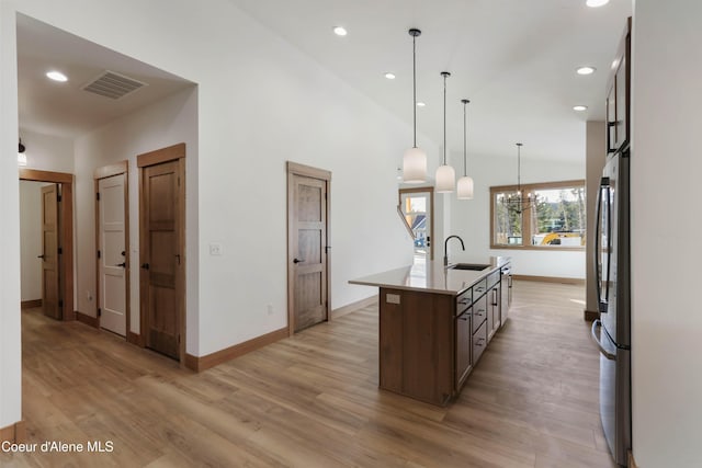 kitchen featuring light wood-style flooring, a kitchen island with sink, a sink, visible vents, and light countertops