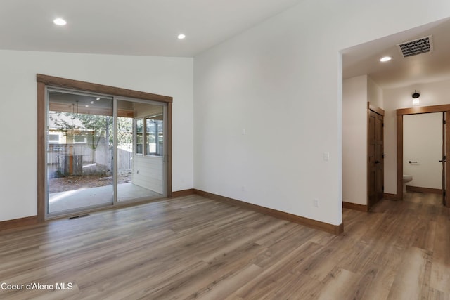 empty room featuring vaulted ceiling, light wood-style flooring, visible vents, and baseboards