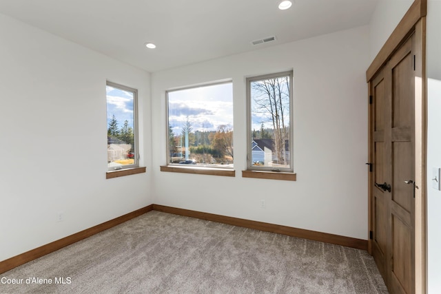 empty room featuring carpet, baseboards, visible vents, and a wealth of natural light