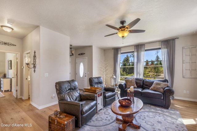 living room with light wood-type flooring, a textured ceiling, baseboards, and a ceiling fan