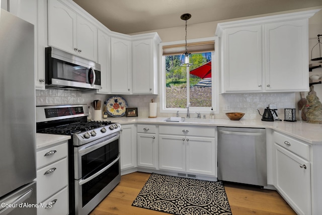 kitchen with stainless steel appliances, white cabinetry, light wood-style floors, and tasteful backsplash