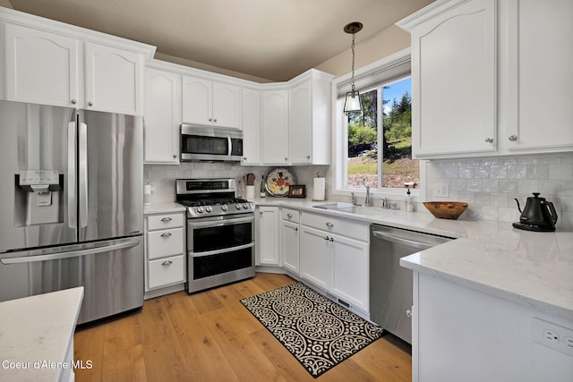 kitchen with stainless steel appliances, backsplash, light wood-style floors, white cabinetry, and a sink