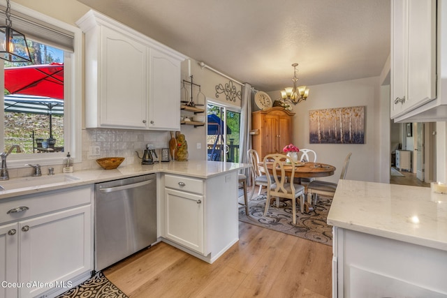 kitchen with a chandelier, white cabinets, stainless steel dishwasher, light wood-type flooring, and backsplash