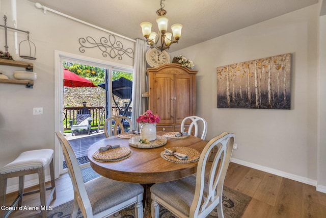 dining area with baseboards, hardwood / wood-style floors, and an inviting chandelier