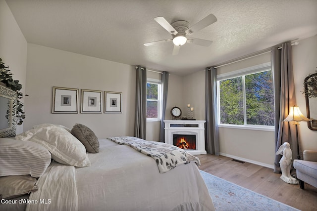 bedroom with a textured ceiling, light wood-style flooring, visible vents, baseboards, and a lit fireplace