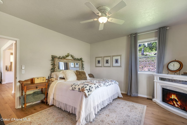 bedroom with a textured ceiling, a lit fireplace, baseboards, and wood finished floors