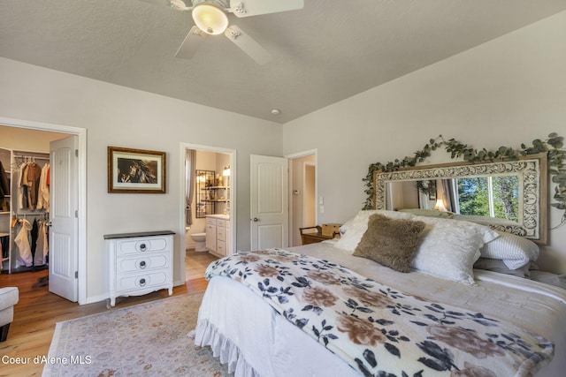 bedroom with a ceiling fan, ensuite bath, wood finished floors, a spacious closet, and a closet