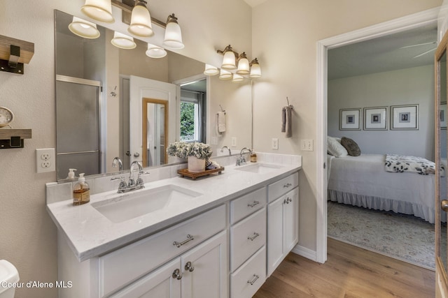 ensuite bathroom with double vanity, a shower stall, a sink, and wood finished floors