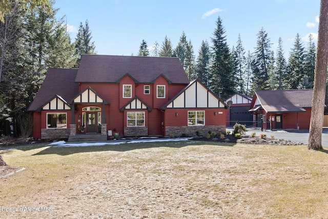 rear view of house with stone siding, roof with shingles, and a yard