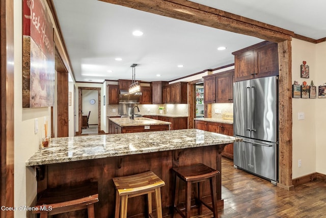 kitchen with a peninsula, high end refrigerator, light stone countertops, dark wood-style floors, and tasteful backsplash