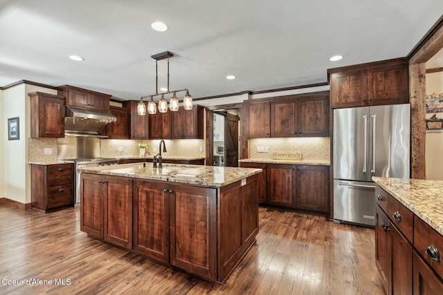 kitchen featuring a barn door, under cabinet range hood, stainless steel appliances, a sink, and dark wood-style floors