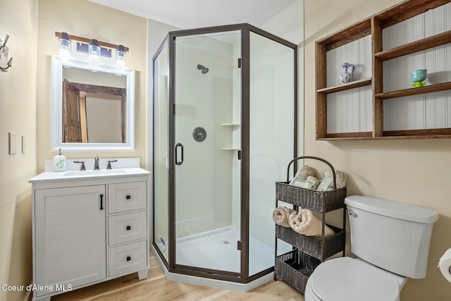 bathroom with toilet, a stall shower, wood finished floors, and vanity