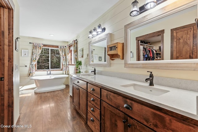 bathroom with wood-type flooring, a sink, a freestanding bath, and double vanity