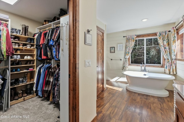 bathroom featuring a walk in closet, a freestanding bath, and wood finished floors