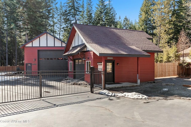 view of front of home with roof with shingles, a fenced front yard, a detached garage, and an outdoor structure