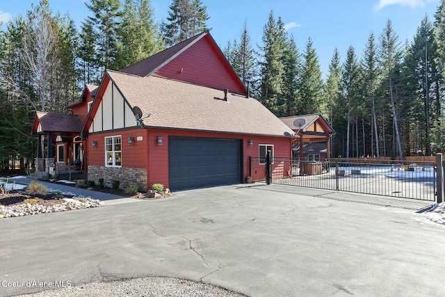 view of side of property with a garage, driveway, stone siding, roof with shingles, and fence