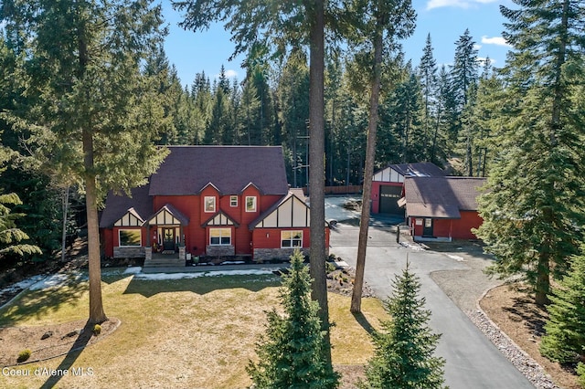 tudor home featuring an outbuilding, a shingled roof, board and batten siding, a garage, and a front lawn