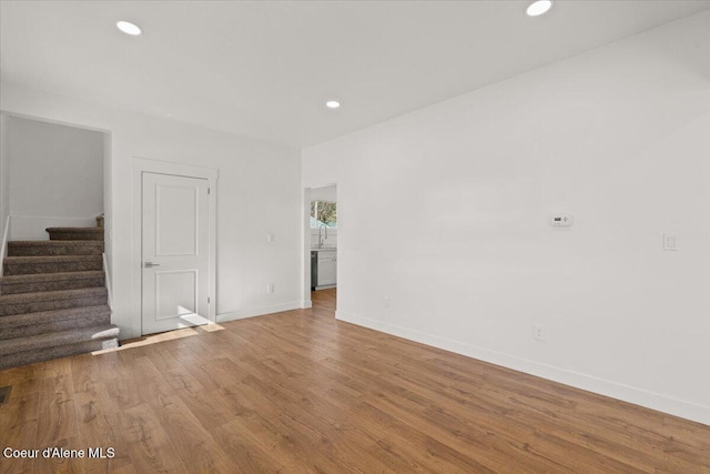 unfurnished room featuring recessed lighting, wood finished floors, baseboards, and stairs