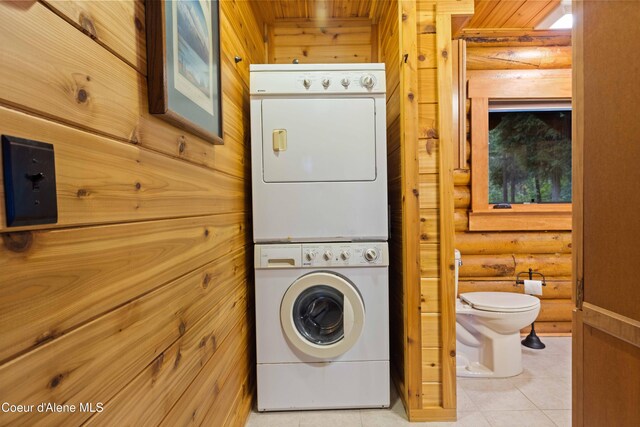 laundry area with laundry area, log walls, stacked washing maching and dryer, and light tile patterned floors