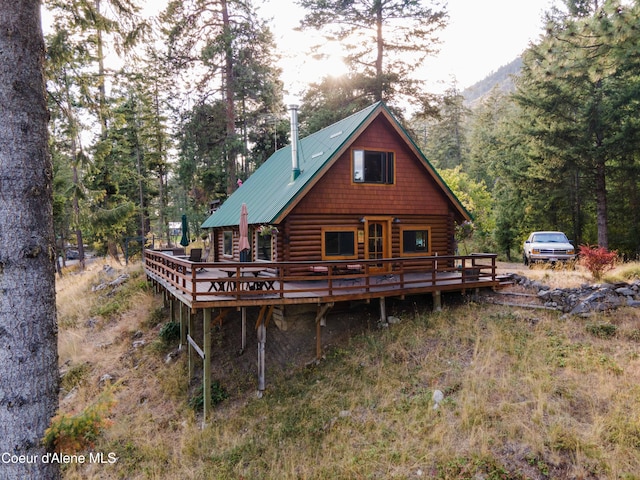 back of house with metal roof, log siding, a wooden deck, and a view of trees