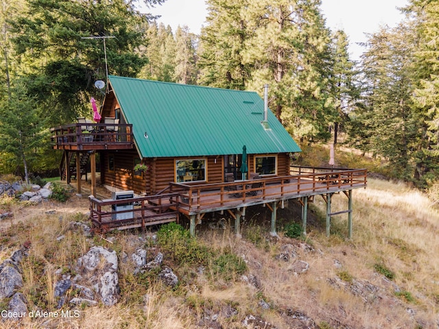 rear view of house with metal roof, a forest view, log siding, and a wooden deck