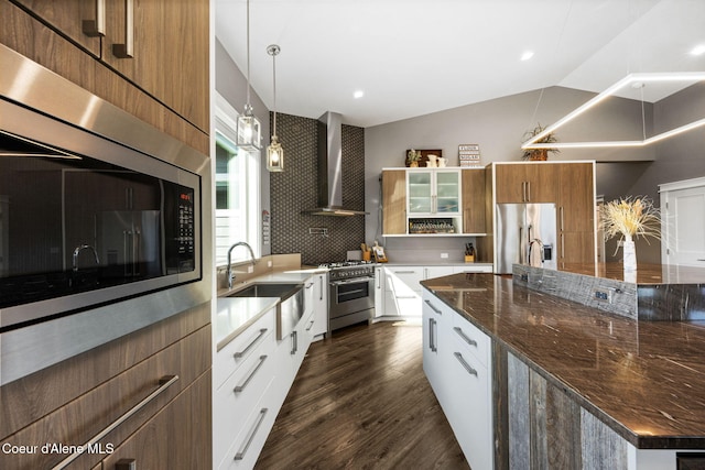 kitchen with high end appliances, a spacious island, a sink, vaulted ceiling, and wall chimney range hood