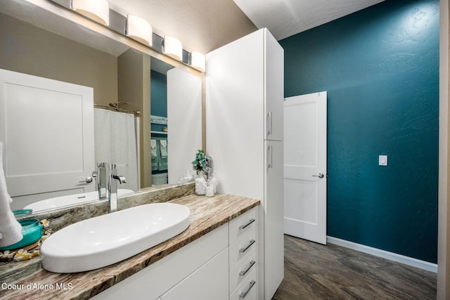 bathroom featuring a shower with curtain, wood finished floors, baseboards, vanity, and a textured wall