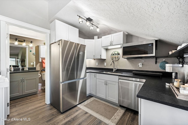 kitchen with a sink, stainless steel appliances, vaulted ceiling, a textured ceiling, and dark countertops