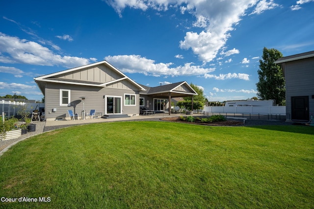 rear view of house with a yard, a patio area, board and batten siding, and a fenced backyard