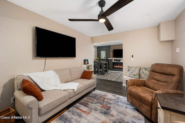 living area featuring a glass covered fireplace, wood finished floors, and ceiling fan