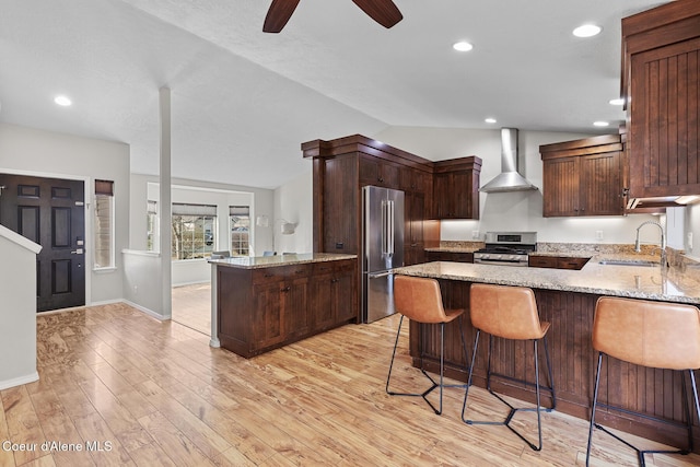 kitchen with light stone counters, stainless steel appliances, a peninsula, a sink, and wall chimney range hood