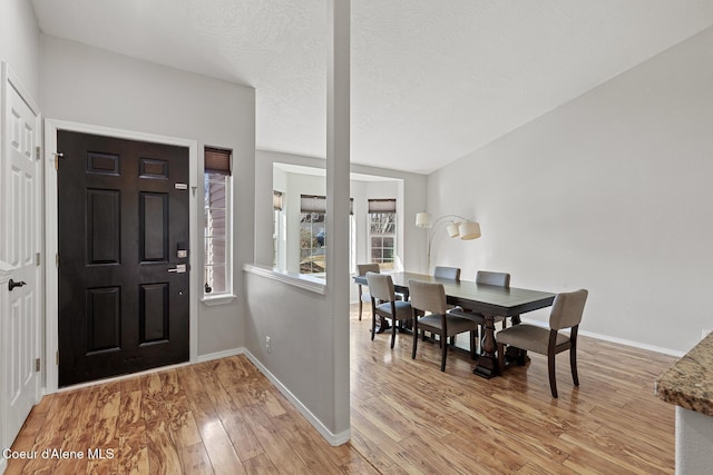 foyer entrance with light wood-style flooring, baseboards, and a textured ceiling