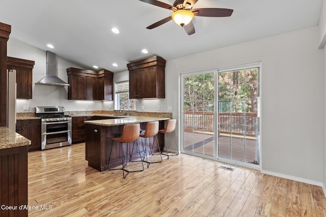 kitchen featuring light wood-style floors, vaulted ceiling, wall chimney range hood, freestanding refrigerator, and double oven range