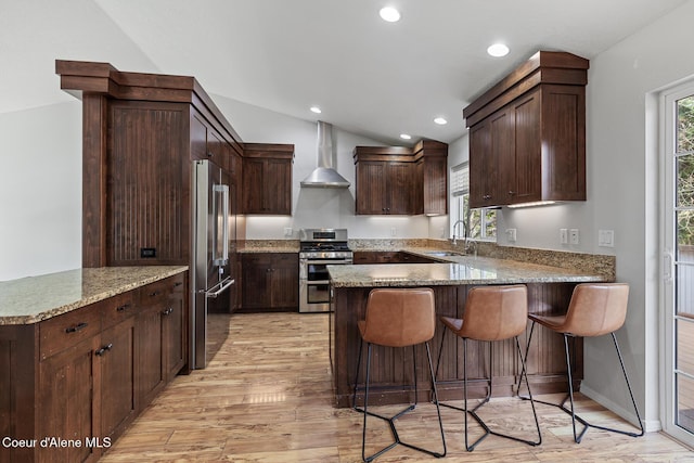 kitchen with stainless steel appliances, a sink, wall chimney range hood, and a peninsula