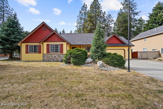 craftsman-style home featuring a front yard, fence, concrete driveway, a garage, and stone siding