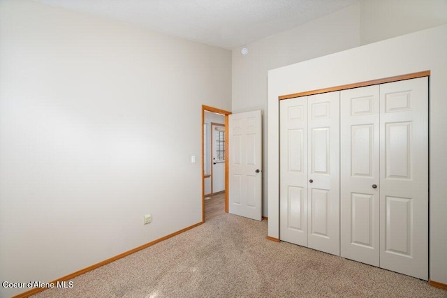 unfurnished bedroom with baseboards, carpet floors, a closet, and vaulted ceiling