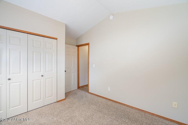 unfurnished bedroom with vaulted ceiling, light colored carpet, a closet, and baseboards