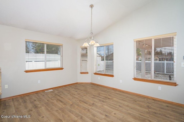 empty room featuring lofted ceiling, wood finished floors, visible vents, and a chandelier