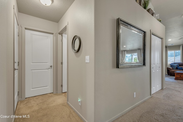 hall with light colored carpet, a textured ceiling, and baseboards