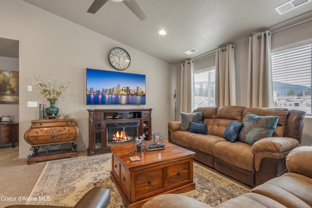 carpeted living room featuring a glass covered fireplace, lofted ceiling, visible vents, and ceiling fan