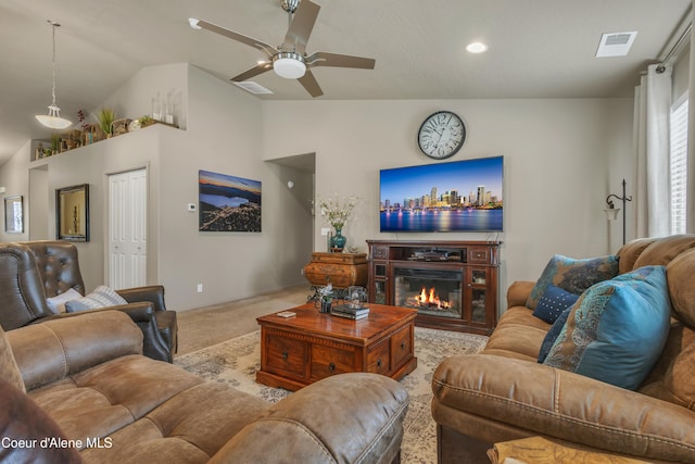 carpeted living room with visible vents, lofted ceiling, a glass covered fireplace, and a ceiling fan