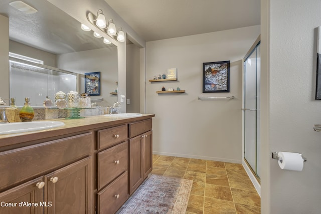 full bathroom featuring double vanity, a stall shower, baseboards, and a sink