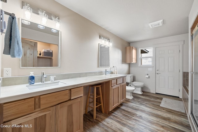 bathroom with toilet, an enclosed shower, a sink, wood finished floors, and double vanity