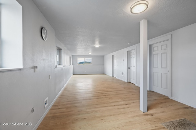 below grade area with a textured ceiling, baseboards, and light wood-type flooring